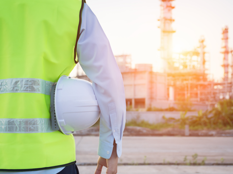 Engineer in safety vest holding hard hat at industrial site